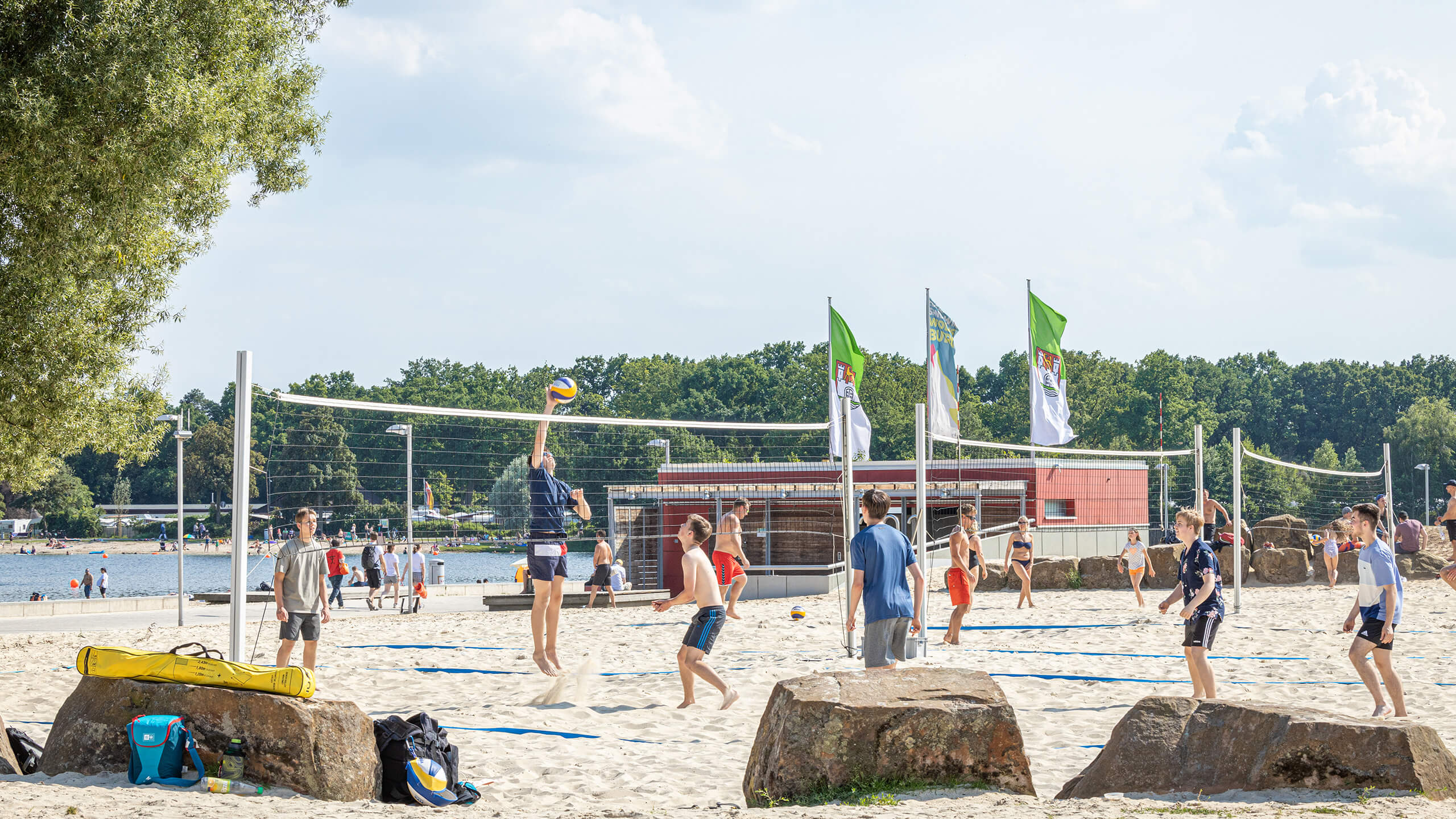 Beachvolleyballfelder im Allerpark mit Spielern, im Hintergrund der Allersee und Bäume.