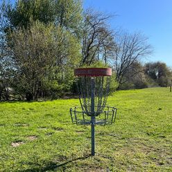 Discgolfkorb auf einer Wiese mit Bäumen im Hintergrund