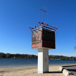 Rettungsturm des DLRG am Strand des Allersees, im Hintergrund der See und das gegenüberliegende Ufer.