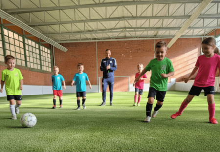 Kinder spielen in einer Halle auf einem Kunstrasen Fußball.