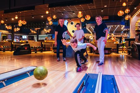 Ein Junge wirft eine Bowlingkugel, im Hintergrund die Familie.