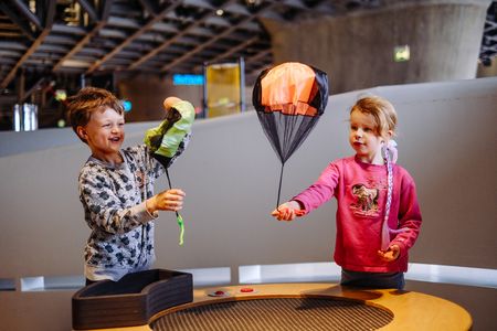 Zwei Kinder halten einen Mini Fallschirm in den Händen über einem Tisch.