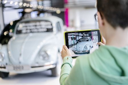 Ein Junge fotografiert mit einem Tablet einen VW Käfer.