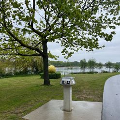 Skulptur eines Planeten am Allersee mit Bäumen und Allersee im Hintergrund.