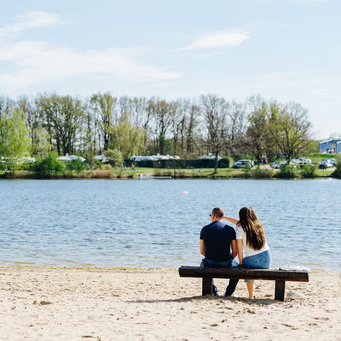 Pärchen sitzt auf einer Bank am Strand des Allersees und blickt auf den See.