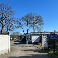 Gepflasterte Einfahrt mit Häusern und Bäumen im Hintergrund.