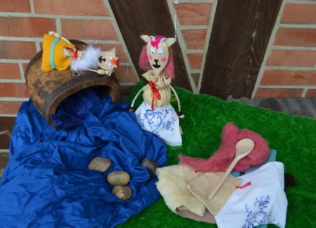 auf einer grünen Stoffunterlage liegen Materialien zum Bau einer Handpuppe. Verschiedene Stoffe, ein Kochlöffel und zwei fertige Handpuppen.