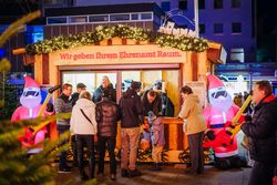 Einige Personen stehen vor einer Holzhütte.